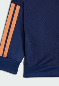 Námornícky športový top z textúrovanej látky s oranžovými trojpruhmi na rukávoch a rebrovaným lemom.