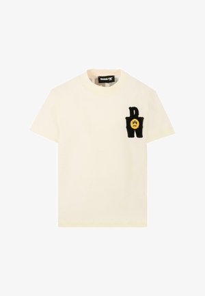 Kremowa bawełniana koszulka z krótkim rękawem, okrągłym dekoltem i filcową aplikacją z czarną literą "P" oraz żółtą buźką na lewej piersi.