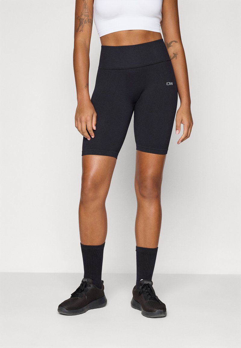 Zwarte ribbelige fietsshorts met een hoge taille, voorzien van een elastische tailleband. Gecombineerd met een witte crop top en zwarte sokken.