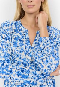 Niebieska bluzka w kwiatowy wzór, wykonana z lekkiego materiału, z zapięciem na guziki z przodu, okrągłym dekoltem i marszczonymi rękawami.