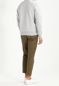 Felpa grigia chiara con trama a maglia, scollatura rotonda e polsini a costine. Pantaloni verde oliva con vestibilità affusolata, abbinati a sneakers bianche.