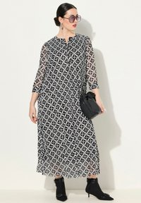 Robe longue à motifs noirs et blancs avec des manches trois-quarts, un devant à boutons et des plis. Portée avec un sac noir et des bottines.