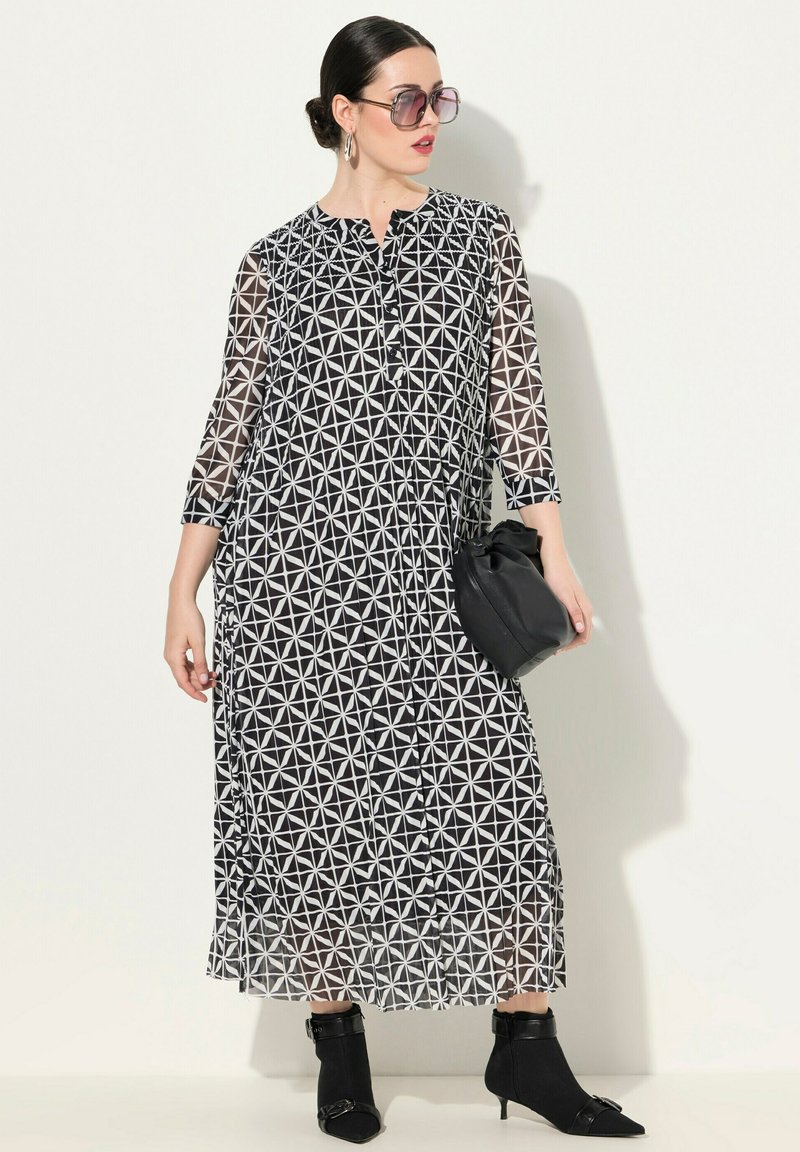 Robe longue à motifs noirs et blancs avec des manches trois-quarts, un devant à boutons et des plis. Portée avec un sac noir et des bottines.