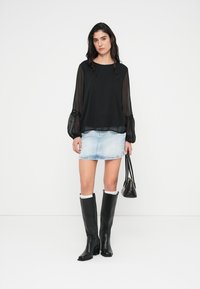 Μαύρη διαφανής μπλούζα με μακριά μανίκια και ελαστικές μανσέτες, συνδυασμένη με φούστα μίνι από γαλάζιο τζιν και μαύρες δερμάτινες μπότες μέχρι το γόνατο. Μαύρη τσάντα χειρός.