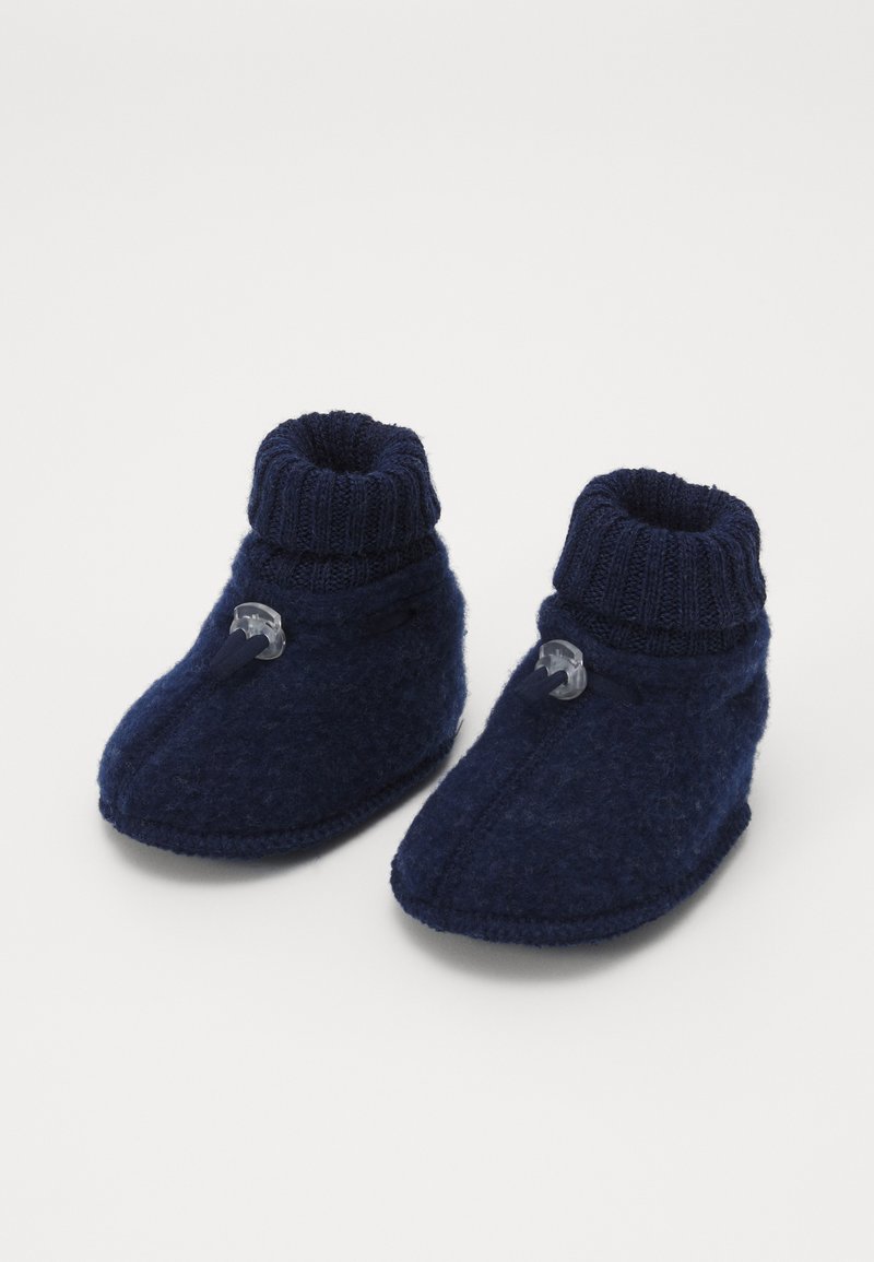Botines de fieltro azul marino con puño de punto acanalado, botón decorativo y detalles cosidos. Textura suave, diseño de punta cerrada para mayor calidez.