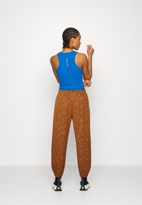 Niebieska bezrękawnik z logo na plecach, zestawiony z luźnymi brązowymi spodniami z teksturowanym wzorem zwierzęcym i elastycznymi mankietami.