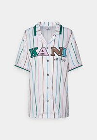 Kratak rukav košulja s gumbima u bijeloj boji s višebojnim vertikalnim prugama. Sadrži izvezeni detalj s logotipom "KANI" i "osn. 1989".