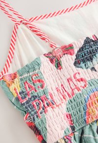 Gros plan d'une robe en tissu smocké colorée avec des bretelles rayées rouges et blanches nouées en un nœud en haut.