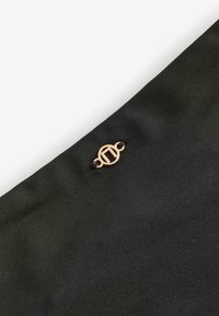 Zwarte stoffen pouch met een textuur, versierd met een klein gouden embleem en een zwart koordje aan de bovenrand.