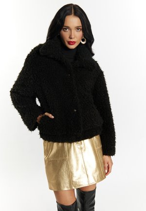 Schwarze, flauschige, kurze Jacke mit Kragen und Knöpfen. Kombiniert mit einem glänzenden goldenen Miniröcken und schwarzen Overknee-Stiefeln.