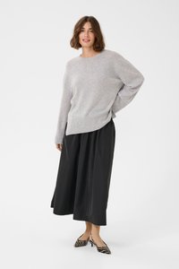 Svetlo sivi oversize pulover s okruglim izrezom, kombiniran s crnom plisiranom suknjom i crno-bijelim cipelama na visoku petu sa prugama.