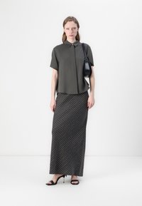 Camicia verde oliva a maniche corte con bottoni, abbinata a una gonna lunga a strisce scure. Borsa nera e tacchi a strappo.