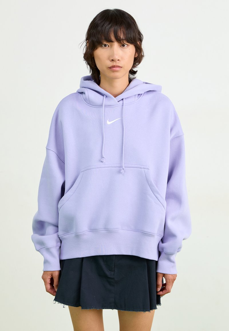 Sweatshirt roxa feito de material suave, com um bolso frontal, capuz com cordão e logótipo branco da Nike no peito. Combinado com uma saia preta.