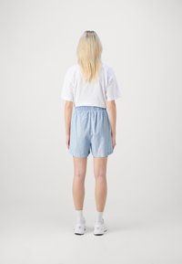 Shorts rayés bleu clair avec une taille élastique, associés à un t-shirt blanc à manches courtes. Le mannequin se tient de dos par rapport à l'objectif.