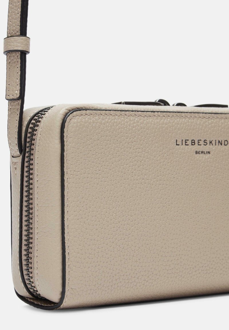 Beige Lederbrieftasche mit strukturierter Oberfläche, einem braunen Reißverschluss und schwarzem Rand. Verfügt über einen abnehmbaren Riemen und ein prägtes Logo auf der Vorderseite.