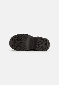 Sorte gummistøvelsåle med dype spor og rund form. Har preget logo og distinkt mønster for bedre grep.