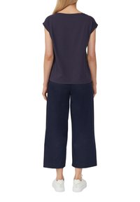 Marineblaues kurzärmliges Oberteil mit rundem Ausschnitt, kombiniert mit weiten marineblauen Hosen. Das Model trägt weiße Sneakers mit strukturiertem Design.
