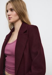 Burgunderfarbener Wollmischung-Überwurf-Blazer mit breiten Revers, einem einzigen Knopfverschluss und strukturierten Schultern, über einem taillierten rosa Top.