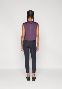 Lila, ujjatlan cropped felső, amelyen az "ELLESSE" logó található, fekete leggingssel párosítva. Az anyag simának és rugalmasnak tűnik, így karcsú sziluettet alakít ki.