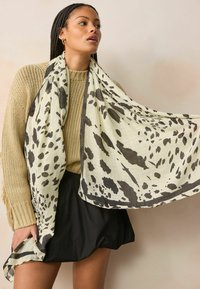 Écharpe légère couleur crème avec des taches abstraites noires, présentant un motif texturé et une bordure noire contrastante.