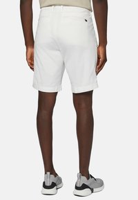 Shorts en coton blanc avec une coupe ajustée, ourlet replié et poches arrière, associés à des chaussures de sport grises. Texture plate, design minimal.