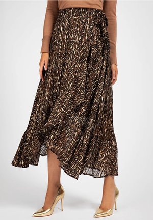 Kvinde iført en flydende, asymmetrisk brun mønstret nederdel med flæsekant, kombineret med guld høje hæle og en brun bluse med lange ærmer.