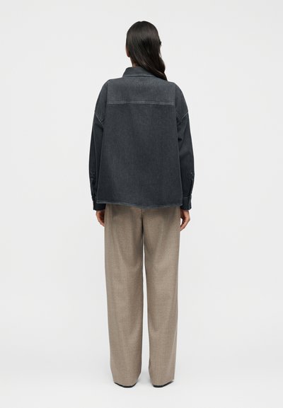 Υπερμεγέθη μαύρο τζιν μπουφάν με γιακά, χαλαρούς ώμους και ορατές ραφές, σε συνδυασμό με μπεζ παντελόνια φαρδιάς γραμμής.