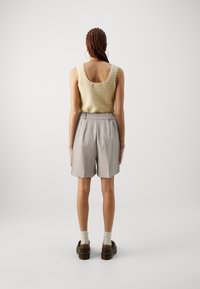 Débardeur en tricot beige avec des bords festonnés, associé à un short taillé gris clair. Chaussures brunes à semelles épaisses et chaussettes blanches.
