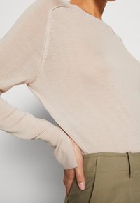 Hellbeige Pullover mit langen Ärmeln, strukturiertem Rippenmuster und Rundhalsausschnitt. Verfügt über leicht taillierte Ärmel und eine geschmeidige Silhouette.