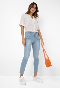 Lichtgewicht, witte linnen shirt met korte mouwen en een knoopsluiting aan de voorkant. Draag het met lichtblauwe gestreepte jeans en een oranje geweven handtas.