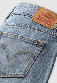 Jean en denim bleu clair plié, montrant la poche arrière avec une couture orange et une étiquette de marque en cuir marron Levi Strauss & Co.