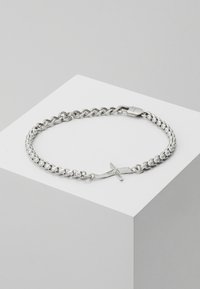 Pulsera de cadena de plata con eslabones entrelazados, una textura suave y un diseño de cierre único con forma de cruz.