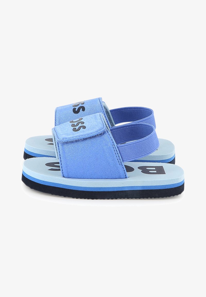 Blå stoffsandaler med borrelåslukking og elastisk hælrem. Lys blå fotseng med en mørk blå såle og svarte logodetaljer.