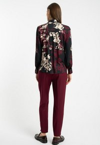Bluzka w kwiatowy wzór w kolorze czarnym, burgundowym i kremowym; długie rękawy, mankiety na guziki; zestawiona z burgundowymi spodniami i błyszczącymi czarnymi butami.
