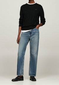 Schwarzer Kabelstrickpullover, lässige Passform, kombiniert mit hellblauen geraden Jeans. Schwarze Loafers runden das Outfit ab.