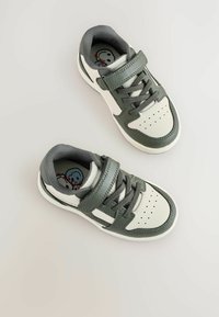 Zielone i białe sneakersy z rzepami i sznurówkami, widziane z góry. Posiadają dekoracyjny wzór wewnątrz buta.