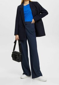 Marinblå oversize-kavaj, blå t-shirt och marinblå byxor med vida ben. Svart handväska med dragkedjor. Vita sneakers. Jämna texturer överallt.