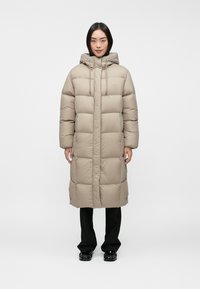 Beige puffer coat with a hood, featuring a quilted design and front closure, paired with black pants and glossy shoes.