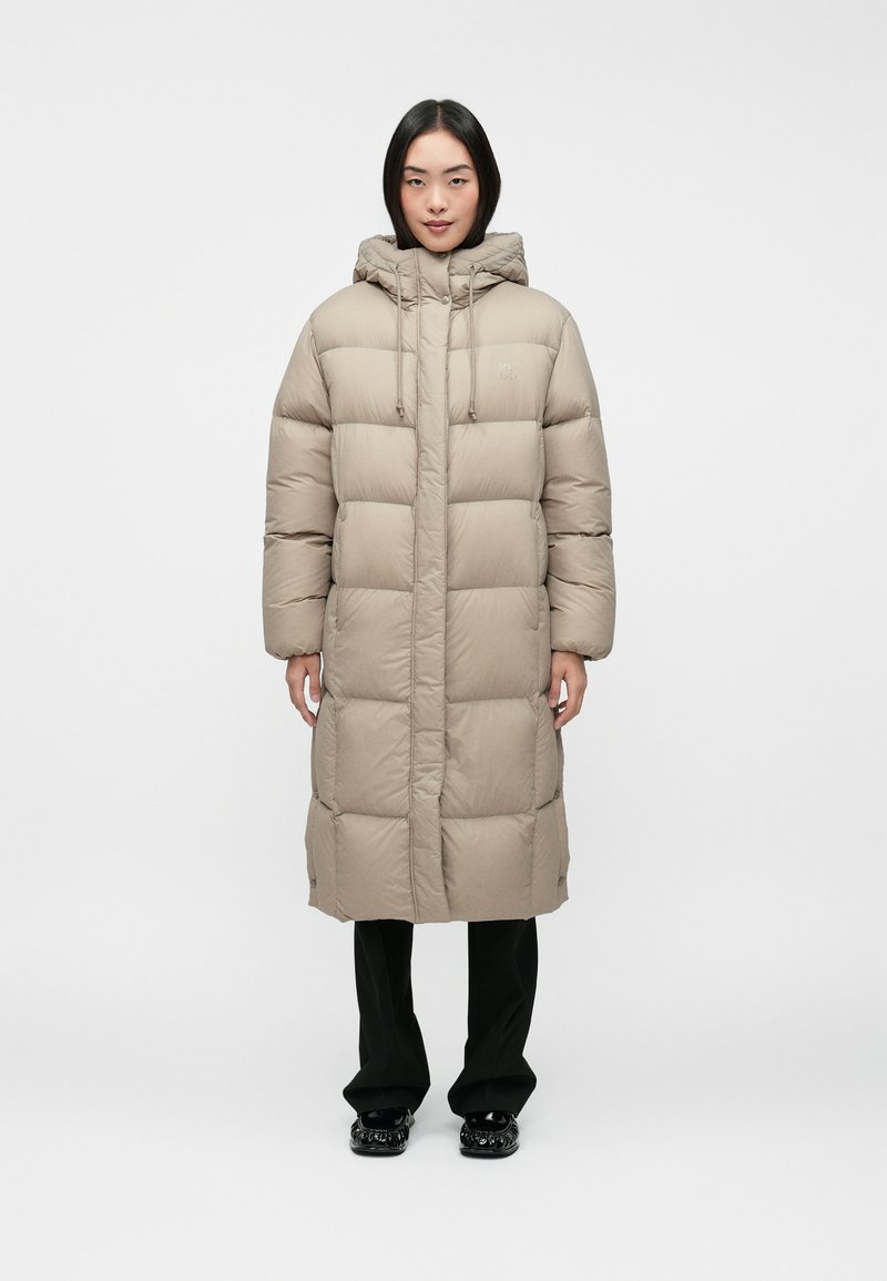 Beige puffer coat with a hood, featuring a quilted design and front closure, paired with black pants and glossy shoes.