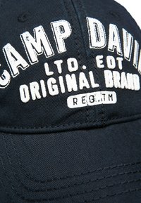Black baseball cap with white embroidered text reading "CAMP DAVID. LTD. EDT. ORIGINAL BRAND." Text has a textured appearance, with a curved brim.