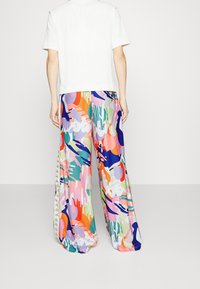 Camiseta blanca de corte relajado y mangas cortas combinada con pantalones de pierna ancha y coloridos que presentan patrones abstractos en rosa, azul, verde y naranja.