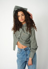 Green patterned cropped shirt with a collared neckline and button closure, paired with high-waisted blue denim jeans.