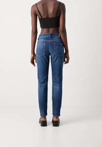 Jeans ajustados de mezclilla azul oscuro, con una cintura de altura media, bolsillos traseros con detalles de costura y un tobillo ajustado. Combinados con un top corto negro.