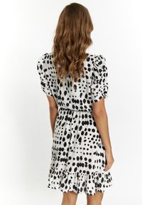 Musta-valkoinen pilkullinen mekko puffihihnoilla, istuvalla bodysuunnittelulla ja röyhelöhännällä. Sileä kangas, keskipitkä malli.