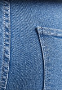 Närbild av ljusblå denimtyg med detaljerad sömnad och det övre hörnet av en rektangulär bakficka.