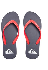 Sandales noires avec des sangles en caoutchouc rouge, semelle texturée et logo blanc. Design de tongs simple, adapté à une tenue décontractée.