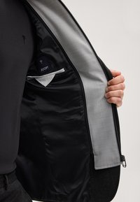 Schwarze Jacke mit einem glatten, dunklen Innenfutter und einem grauen Stoffakzent. Enthält eine Tasche mit dem Aufdruck "JOOP!" und einen Reißverschluss.