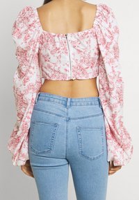 Crop top blanc avec motif floral rouge, manches ballon et fermeture éclair au dos ; associé à un jean en denim léger bleu ciel taille haute avec poches arrière.
