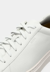 Weiße Ledersneaker mit strukturiertem Finish, runder Zehenform, Schnürdesign und dezentem "BOSS" Branding an der Seite. Minimalistische Ästhetik.