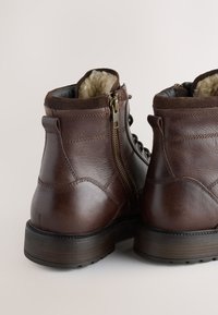Braune Leder-Stiefeletten mit Reißverschluss, strukturierter Oberseite und kontrastierenden glatten Akzenten. Dicke Gummisohle für Haltbarkeit und Grip.